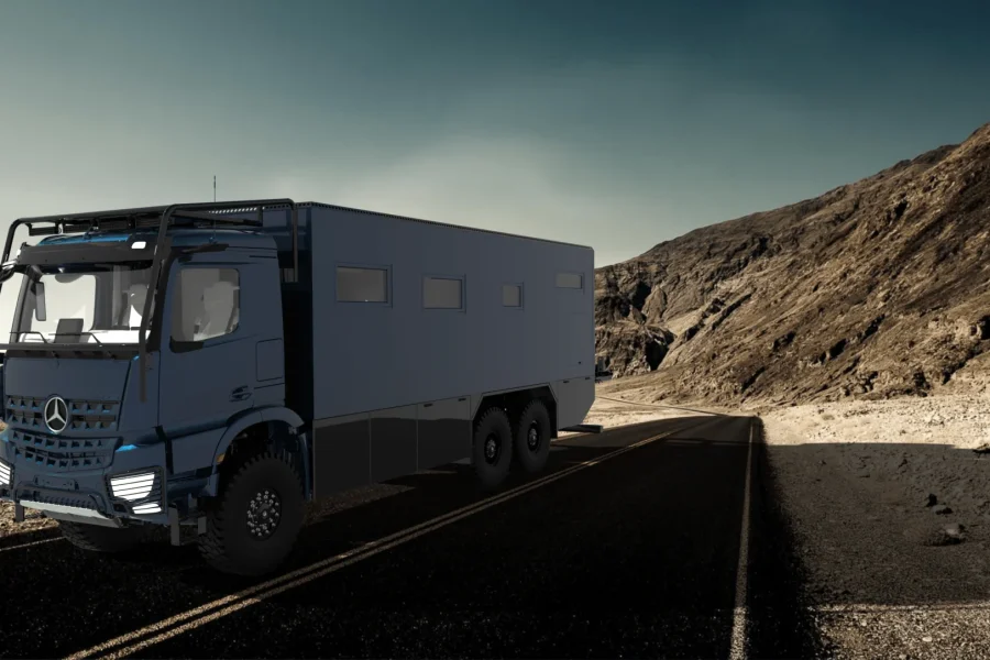 Un camion Mercedes bleu avec une grande caisse se dresse sur une route asphaltée dans un paysage désertique avec des montagnes nues et brunes en arrière-plan sous un ciel nuageux.