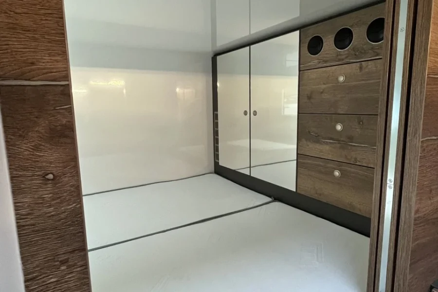 紧凑的睡眠舱配有白色床垫，周围是白灰色的墙壁和木质镶板，右侧有凹进的隔间和抽屉。
