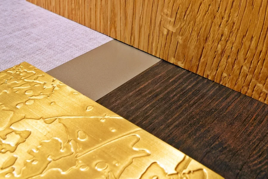Nahaufnahme von vier verschiedenen Materialien: ein goldenes, strukturiertes Metall, ein glattes hellbraunes Material, dunkles Holz und helles Holz mit sichtbarer Maserung.