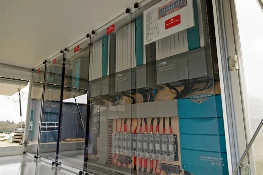 Innenansicht eines elektrischen Schaltschrankes mit mehreren blauen und grauen Steuergeräten und transparenten Abdeckungen in einem weißen Gehäuse.